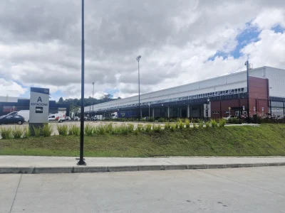 Vista de fachada do Bloco 200 de galpões modulares. Em primeiro plano final da rampa de acesso ao empreendimento, com estacionamento externo logo atrás.